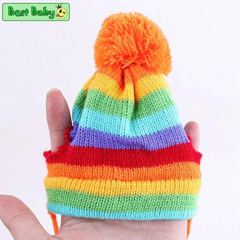 Colorful striped knit pet hat with pom-pom held in hand against a white background.