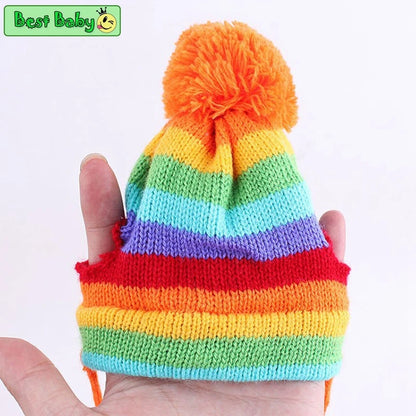 Colorful striped knit pet hat with pom-pom held in hand against a white background.